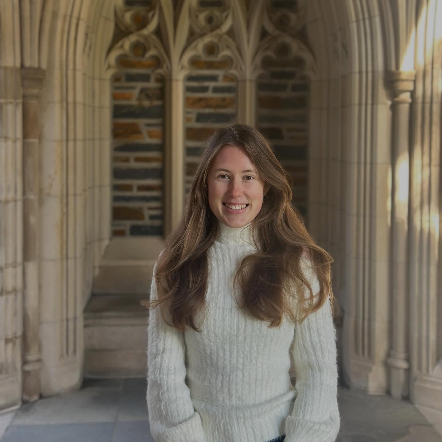 Anastasiia smiling in a white sweater beneath the stone arches at Duke University